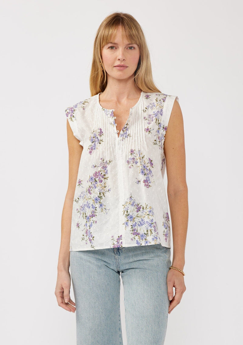 [Color: Off White/Lilac] A front-facing image of a blonde model wearing a white top adorned with a purple floral print and embroidered eyelet accents. This spring top features a button-front neck closure and delicate pintuck details.