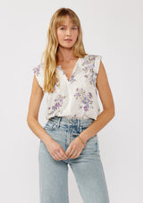 [Color: Off White/Lilac] A front-facing image of a blonde model wearing a white top adorned with a purple floral print and embroidered eyelet accents. This spring top features a button-front neck closure and delicate pintuck details.