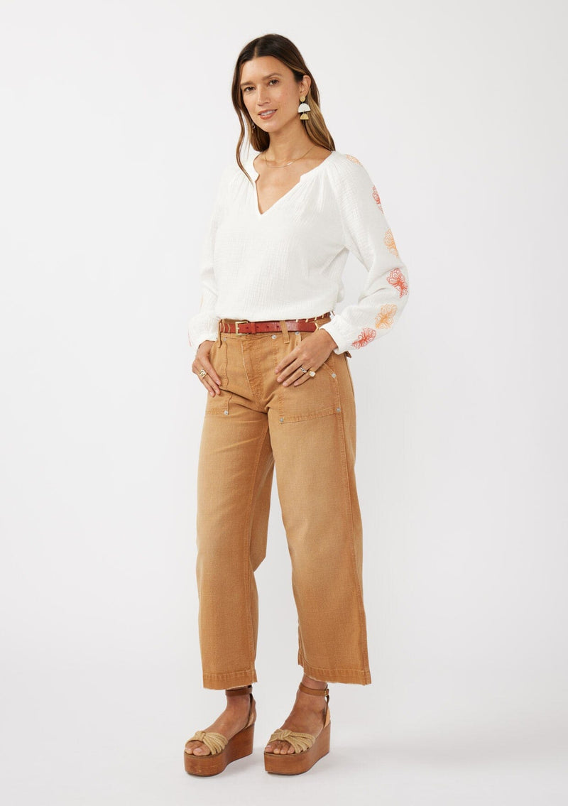 [Color: White/Coral] A front facing image of a brunette model wearing a bohemian cotton white blouse with embroidered details. Featuring a split v-neckline, long sleeves, and button wrist closure.  