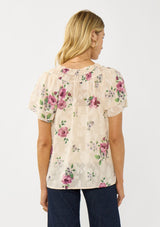 [Color: Natural/Dusty Rose] A back facing image of a blonde model wearing a pretty top with jacquard floral details and a subtle sheen. Featuring a split v-neckline, short flutter sleeves, and a ruffled neckline. 