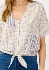 [Color: Oatmeal/Plum] A detail image of a blonde model wearing a boho floral tie front top with short dolman sleeves, a v-neckline, and button front. 