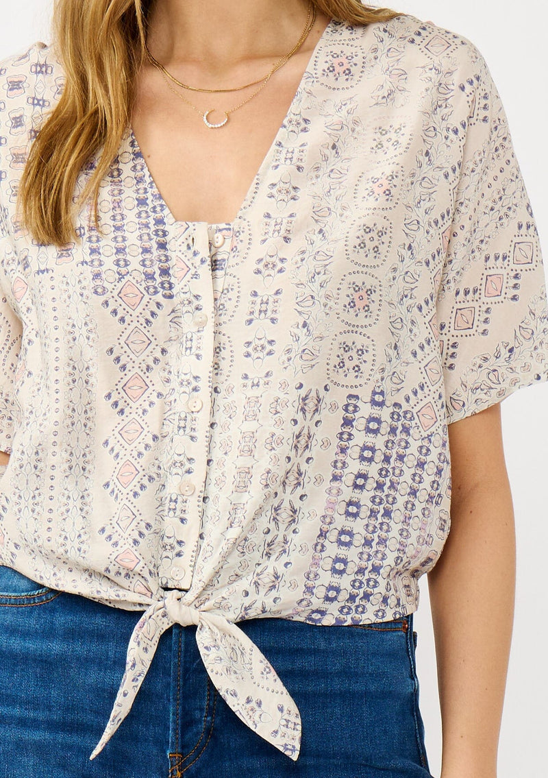 [Color: Oatmeal/Plum] A detail image of a blonde model wearing a boho floral tie front top with short dolman sleeves, a v-neckline, and button front. 