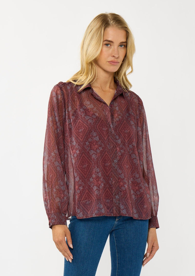 [Color: Wine/Rose] A front facing image of a blonde model wearing a floral diamond print chiffon blouse with metallic thread details. Featuring metallic thread details, a button front, and long sleeves with a tailored cuff. A special occasion top for the fall season. 