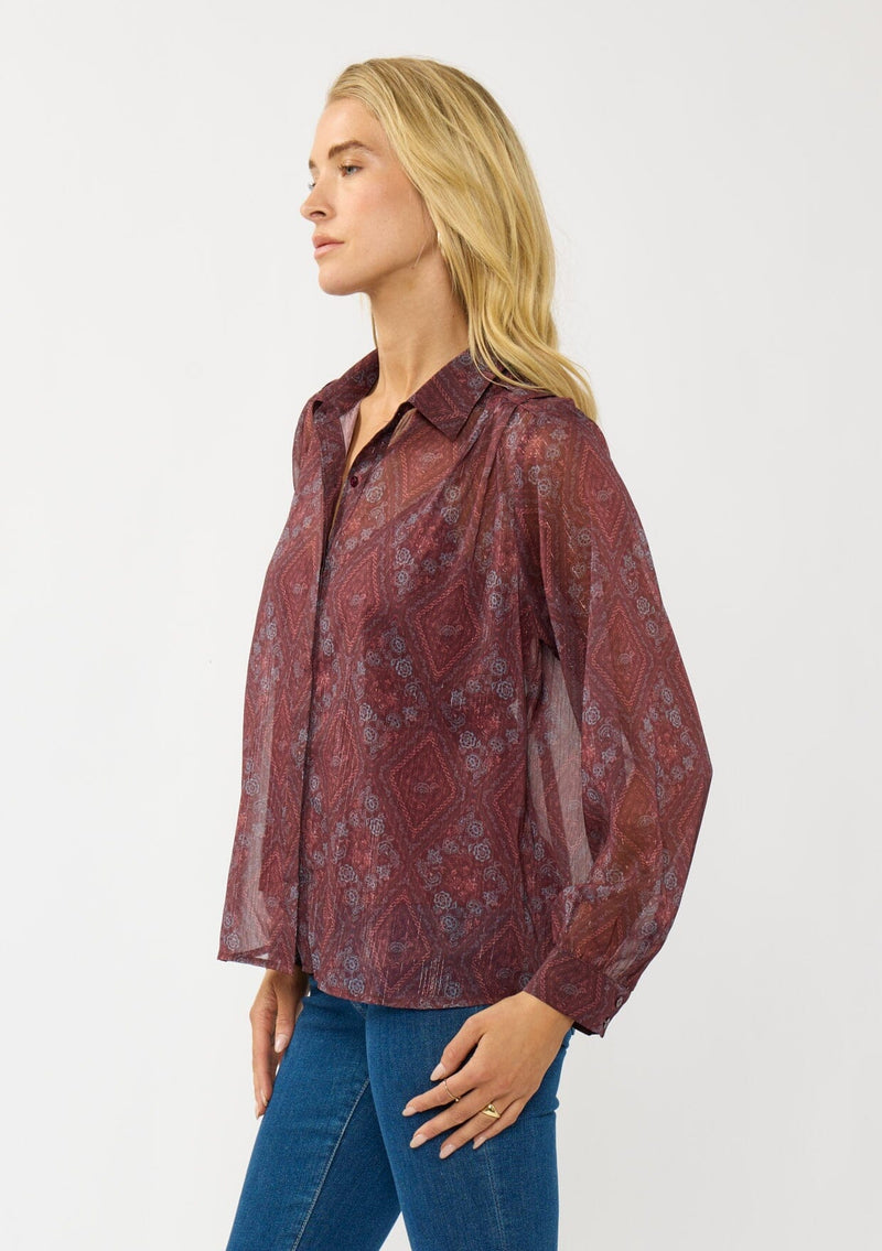 [Color: Wine/Rose] A side facing image of a blonde model wearing a floral diamond print chiffon blouse with metallic thread details. Featuring metallic thread details, a button front, and long sleeves with a tailored cuff. A special occasion top for the fall season. 