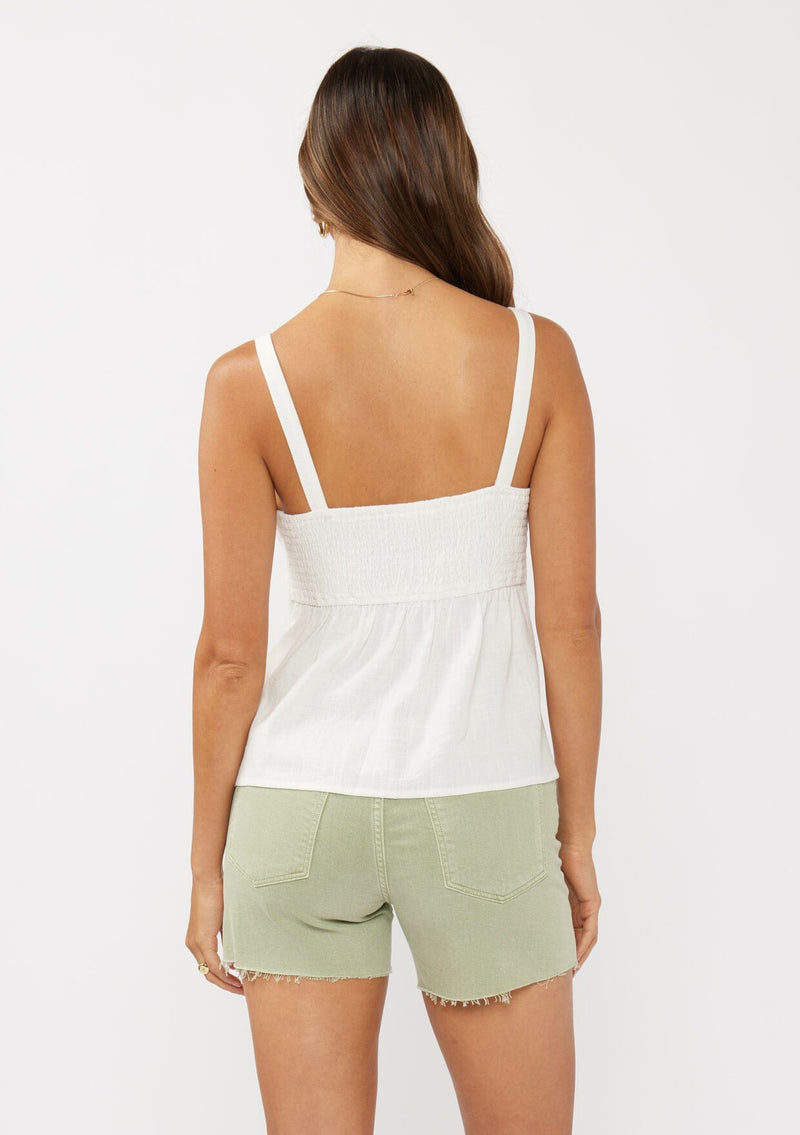 [Color: White] A front facing image of a brunette model wearing a white boho tank top with a smocked back, button front, an eyelet trim, and pintuck details. Perfect for everyday spring styling. 