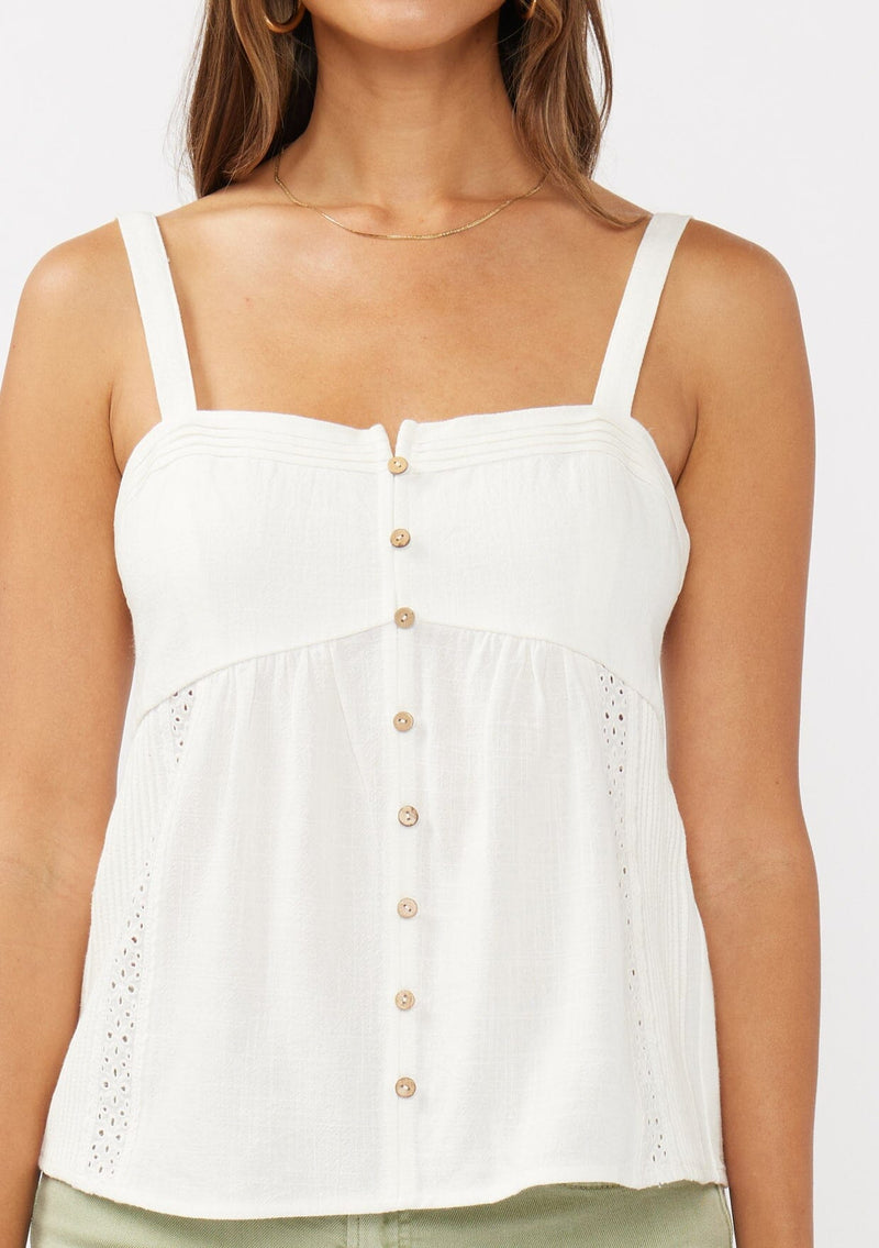[Color: White] A detail image of a brunette model wearing a white boho tank top with a smocked back, button front, an eyelet trim, and pintuck details. Perfect for everyday spring styling. 