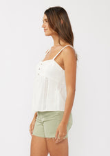[Color: White] A side facing image of a brunette model wearing a white boho tank top with a button front, an eyelet trim, and pintuck details. Perfect for everyday spring styling. 