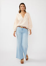 [Color: Peach] A front facing image of a brunette model wearing a light pink blouse with long raglan sleeves, a split v-neckline with button detail, lace inserts, and pintuck details. 