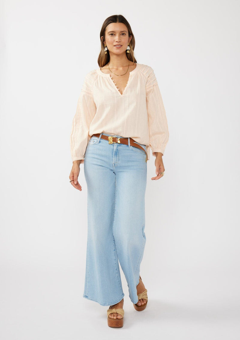 [Color: Peach] A front facing image of a brunette model wearing a light pink blouse with long raglan sleeves, a split v-neckline with button detail, lace inserts, and pintuck details. 