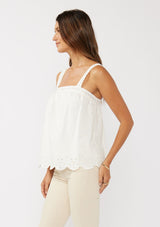 [Color: White] A side facing image of a blonde model wearing a white cotton eyelet tank top with adjustable straps and a scalloped hem. 