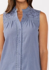[Color: Denim Blue] A detail image of a brunette model wearing a blue classic boho tank top with a button front, embroidered yoke, and lace trim accents. 