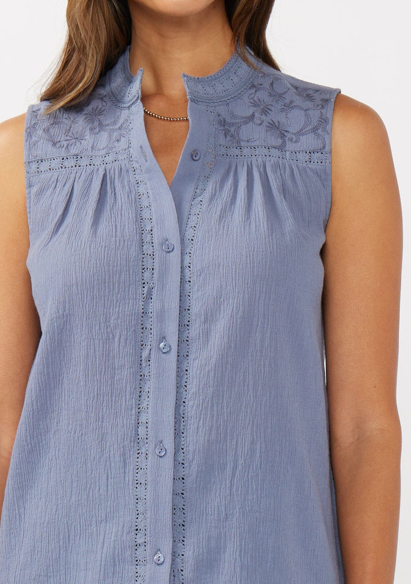 [Color: Denim Blue] A detail image of a brunette model wearing a blue classic boho tank top with a button front, embroidered yoke, and lace trim accents. 