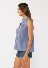 [Color: Denim Blue] A side facing image of a brunette model wearing a blue classic boho tank top with a button front, embroidered yoke, and lace trim accents. 