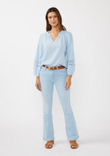 [Color: Chambray Blue] A front facing image of a brunette model wearing a light blue cotton slub blouse with long sleeves, lace details, and a split v-neckline. A versatile boho blouse perfect for the spring season. 
