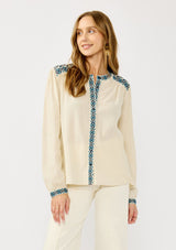 [Color: Vanilla/Dusty Turquoise] A front facing image of a blonde model wearing a cream cotton slub blouse with blue embroidered details, button front, a round neckline, and long sleeves. 