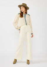 [Color: Vanilla/Dusty Turquoise] A front facing image of a blonde model wearing a cream cotton slub blouse with blue embroidered details, button front, a round neckline, and long sleeves. 
