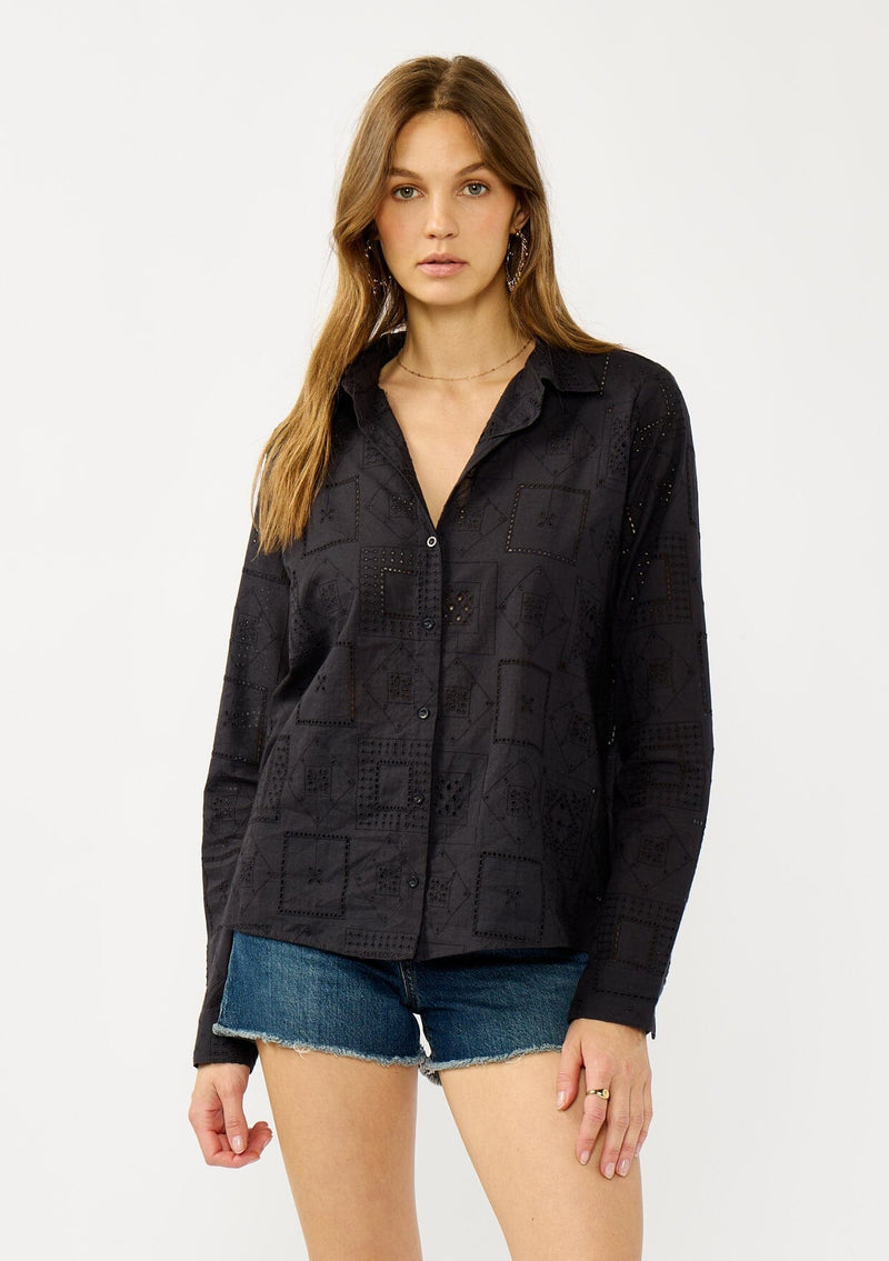 [Color: Graphite] A front facing image of a blonde model wearing a black eyelet shirt with a collared neckline, button front, and button cuff closure.