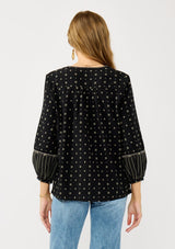 [Color: Black/Taupe] A back facing image of a blonde model wearing a black and taupe cotton jacquard blouse with a split v-neckline, tassel ties, long sleeves, and blanket stitch details. A fall bohemian top. 