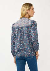 [Color: Teal] A back facing image of a blonde model wearing a blue floral blouse with a button front, quilted yoke detail, and long sleeves. A boho fall blouse for casual outings. 