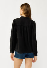 [Color: Black] A back facing image of a blonde model wearing a soft vintage wash black shirt with tonal embroidered details. Featuring a classic collar neckline, button front, and button cuff. 