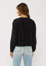 [Color: Black] A back facing image of a brunette model wearing black lightweight blouse with pintuck accents, a button front, and split v-neckline. Airy and sheer for any warm weather occasion. 