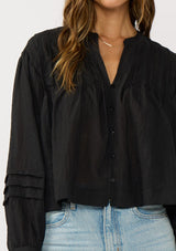[Color: Black] A detail image of a brunette model wearing black lightweight blouse with pintuck accents, a button front, and split v-neckline. Airy and sheer for any warm weather occasion. 