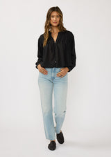 [Color: Black] A front facing image of a brunette model wearing black lightweight blouse with pintuck accents, a button front, and split v-neckline. Airy and sheer for any warm weather occasion. 