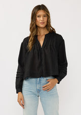 [Color: Black] A front facing image of a brunette model wearing black lightweight blouse with pintuck accents, a button front, and split v-neckline. Airy and sheer for any warm weather occasion. 