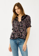 [Color: Black/Pink] A front facing image of a black and pink floral print top with puff sleeves, a split v-neckline with ties, shirred details, and lace trims. A day to night versatile top for the fall season. 