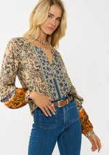 [Color: Natural/Rust] A front facing image of a blonde model wearing a yellow and orange floral blouse with a split v-neckline and long voluminous sleeves. A stunning bohemian fall blouse.