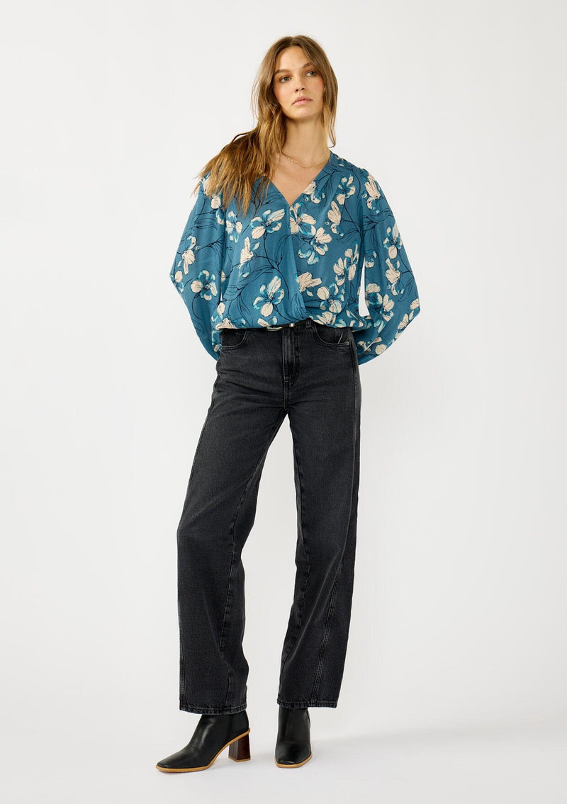 [Color: Teal/Blue] A front facing image of a blonde model wearing a teal floral surplice top with a relaxed fit, long sleeves, front hook and eye, and an elastic hemline. The perfect fall top for casual outings. 