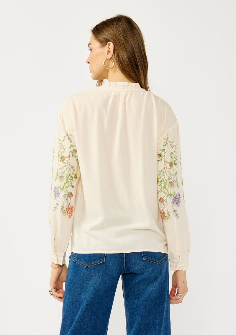 [Color: Stone/Lavender] A back facing image of a blonde model wearing a cream floral blouse with a button front and ruffle trims. A garden style top for special occasions. 