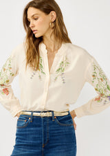 [Color: Stone/Lavender] A front facing image of a blonde model wearing a cream floral blouse with a button front and ruffle trims. A garden style top for special occasions. 