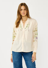 [Color: Stone/Lavender] A front facing image of a blonde model wearing a cream floral blouse with a button front and ruffle trims. A garden style top for special occasions. 