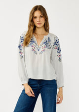 [Color: Light Grey/Navy] A front facing image of a blonde model wearing a light grey blue blouse with floral embroidery, a split v-neckline, and long sleeves with cuffs.  