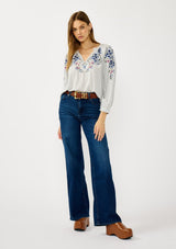 [Color: Light Grey/Navy] A front facing image of a blonde model wearing a light grey blue blouse with floral embroidery, a split v-neckline, and long sleeves with cuffs.  
