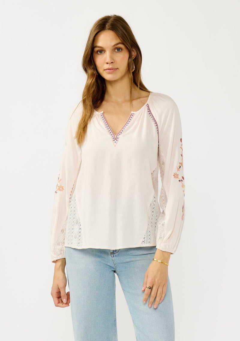 [Color: Pale Rose] A front facing image of a blonde model wearing a light pink blouse with floral embroidery, lace accents, and a flattering split v-neckline. Effortlessly boho and feminine for casual outings. 
