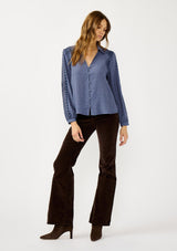 [Color: Denim] A front facing image of a blonde model wearing a blue button up blouse with embroidered details, a collared neckline, and button cuffs. A casual yet elegant top for the fall season. 