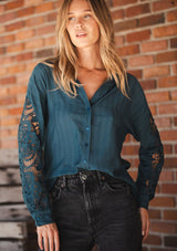 [Color: Teal] A front facing image of a blonde model wearing a striped jacquard teal shirt with lace cutouts, a button front, and collared neckline. A cool and polished blouse for the fall season. 