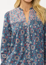 [Color: Teal] A detail image of a blonde model wearing a blue floral blouse with a button front, quilted yoke detail, and long sleeves. A boho fall blouse for casual outings. 