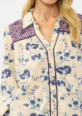 [Color: Cream/Plum] A detail image of a blonde model wearing a purple and cream floral boho shirt with a classic collar neck and button front. A unique fall top for casual styling. 