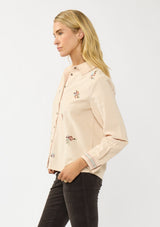 [Color: Vanilla] A side facing image of a blonde model wearing a corduroy shirt with floral embroidery, a button front, and a collar neck. A soft and comfortable shirt for the fall season. 