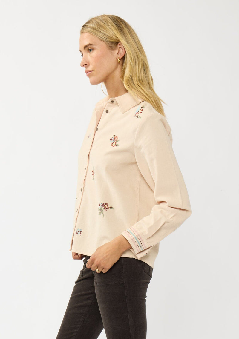 [Color: Vanilla] A side facing image of a blonde model wearing a corduroy shirt with floral embroidery, a button front, and a collar neck. A soft and comfortable shirt for the fall season. 