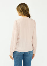 [Color Dusty Rose] A back facing image of a brunette model wearing a satin jacquard blouse with a button front and lace trims. 