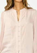 [Color Dusty Rose] A detail image of a brunette model wearing a satin jacquard blouse with a button front and lace trims. 