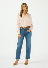 [Color Dusty Rose] A front facing image of a brunette model wearing a satin jacquard blouse with a button front and lace trims. Paired with a dark wash denim, brown belt, and brown suede closed toe heels.