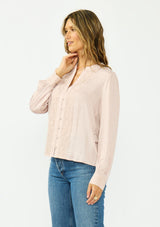 [Color Dusty Rose] A side facing image of a brunette model wearing a satin jacquard blouse with a button front and lace trims. 