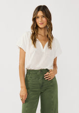 [Color: White] A front facing image of a brunette model wearing a white puff sleeve blouse with an eyelet inspired design and a split v-neckline with ties. 