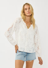 [Color: White] A front facing image of a blonde model wearing a white blouse with a clipped floral design, fuzzy texture, button front, and long sheer sleeves. An everyday warm weather style. 