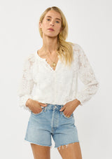 [Color: White] A front facing image of a blonde model wearing a white blouse with a clipped floral design, fuzzy texture, button front, and long sheer sleeves. An everyday warm weather style. 